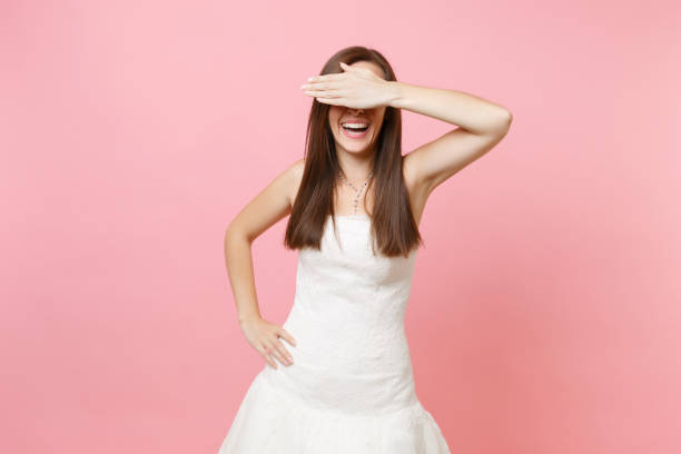 Portrait of laughing bride woman in beautiful lace white wedding dress hiding covering eyes with hand isolated on pastel pink background. Wedding celebration concept. Copy space for advertisement. Portrait of laughing bride woman in beautiful lace white wedding dress hiding covering eyes with hand isolated on pastel pink background. Wedding celebration concept. Copy space for advertisement hair covering eyes stock pictures, royalty-free photos & images