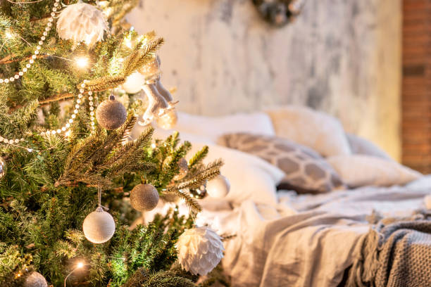 istock Fir Branches decorated in the foreground. Loft apartments, brick wall with candles and Christmas tree. Bed in the bedroom, high large Windows 1074546746