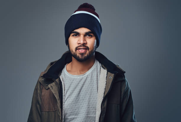Portrait of bearded Indian male dressed in a winter jacket over grey background.