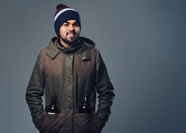 Portrait of bearded Indian male dressed in a winter jacket over grey background.