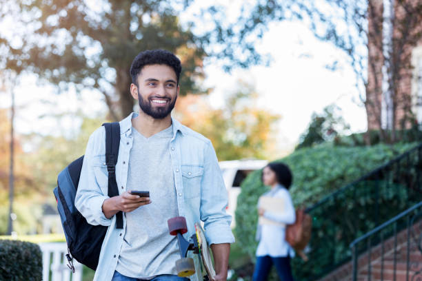 istock Cheerful male college student carries skateboard through campus 1074625068