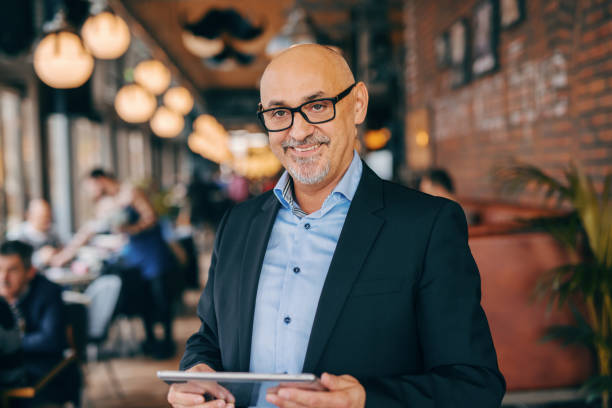 smiling bearded senior in suit using tablet while standing in cafeteria. - mobility working digital tablet people imagens e fotografias de stock