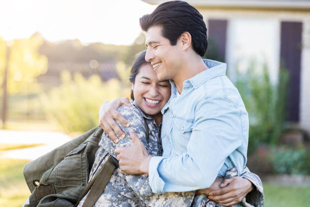 Female in uniform shares a hug with her husband Young, Hispanic female in uniform hugs her husband tightly, after she has just arrived home from duty. She still holds her bag on her shoulder, while they stand outside their home. wife stock pictures, royalty-free photos & images