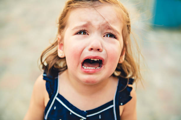 Close up portrait of crying little toddler girl with outdoors background. Child stock photo
