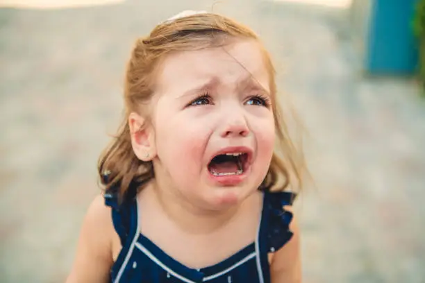 Photo of Close up portrait of crying little toddler girl with outdoors background. Child
