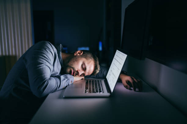 若い白人ビジネスマン夜遅くオフィスで眠っています。彼の横にあるノート パソコン。 - 長い ストックフォトと画像