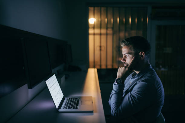 istock Young concerned bearded Caucasian businessman looking at laptop and finding a solution for the problem while sitting late at night in the office. 1074639948