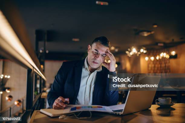 Betroffenen Im Mittleren Alter Geschäftsmann Blick Auf Tabelle Und Halten Stift In Der Hand Beim Sitzen Im Café Am Abend Auf Dem Tisch Kaffee Laptop Und Tagesordnung Stockfoto und mehr Bilder von Alter Erwachsener