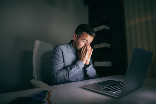 istock Young Caucasian employee blowing nose while sitting in the office late at night. 1074643782