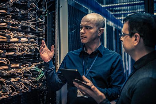 Photo of an IT engineer with a digital tablet explaining server configuration and operation to his supervisor.