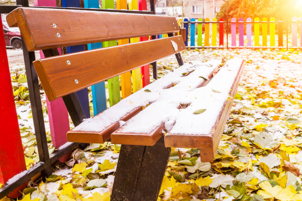 The first snow lies on a wooden bench with backrest and on the yellow and green leaves on the ground, solitude concept The first snow lies on a wooden bench with backrest and on the yellow and green leaves fallen on the ground, solitude concept backrest stock pictures, royalty-free photos & images