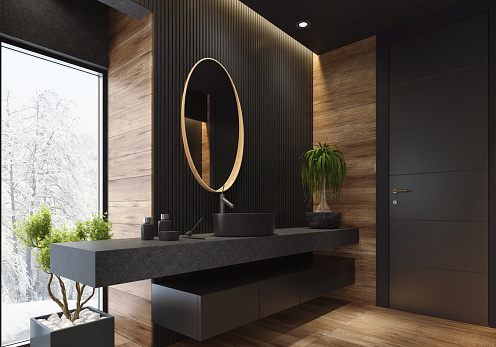 contemporary minimalist bathroom with black wooden walls and large grey matte and wood effect tiles. 
round mirror with wooden frame is on the wooden black wall. 
round grey stone washbasin and stainless steel basin tap is on top of the grey stone vanity unit with three drawers.
freestanding black stone bathtub and floor mounted inox tap is on a platform with wood effect tiles. 
long floor tiles with wood effect. black ceiling with strip cove lighting and embedded spotlights.

***background is my istock image