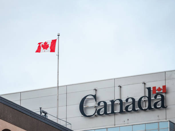Canada Wordmark, the official logo of the Canadian government, on an administrative building next to a Canadian flag waiving stock photo