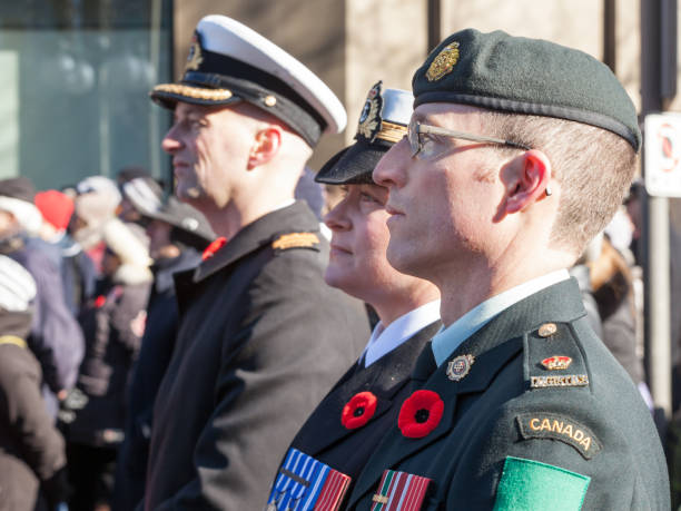 Soldiers from Canadian Army, two men, a woman, from Navy & ground forces, wearing remembrance poppy, standing on ceremony for Remembrance day stock photo