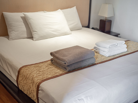 Clean gray and white towels and three white pillows on bed in luxury room in hotel.