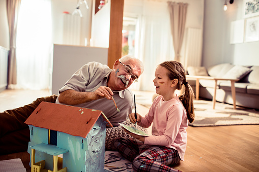 Close up of a little girl coloring a dollhouse with her grandfather