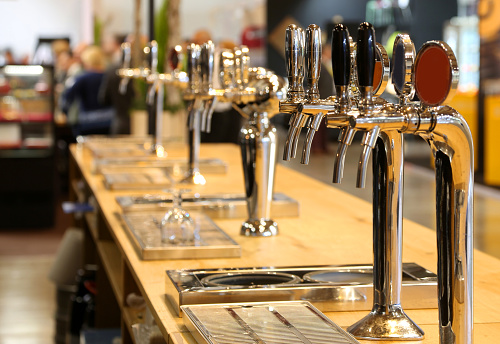 many draft beer taps lined up on the counter of a pub