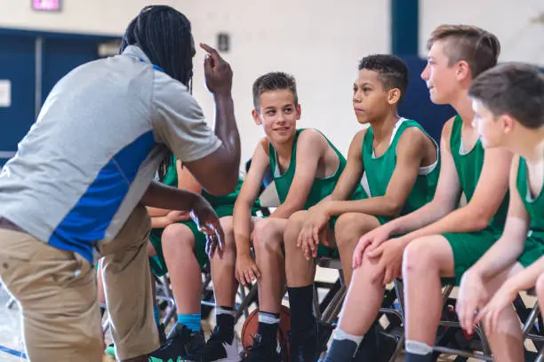 Photo of Elementary boys basketball team sitting on the sideline bench with their coach