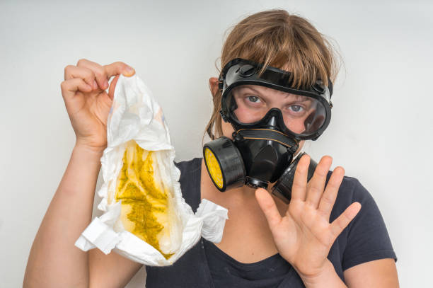 Mother with gas mask changing smelly diaper - baby care concept