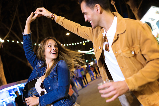 Shot of carefree young couple dancing holding hands in eat market in the street at night.