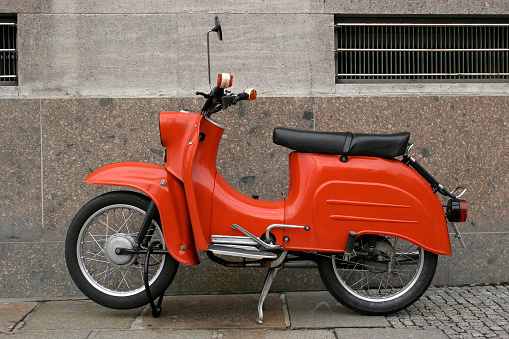 A cool, classic, red vintage scooter with a St Tropez decal parked in the St Tropez harbour area.