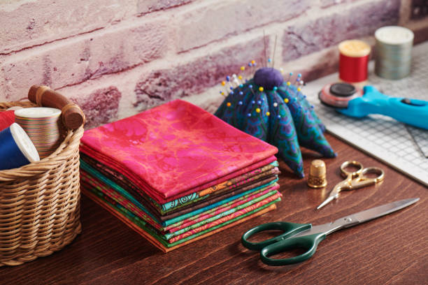 stack of colorful fabrics on table surrounded by sewing accessories on brick wall background - patch textile stack heap imagens e fotografias de stock