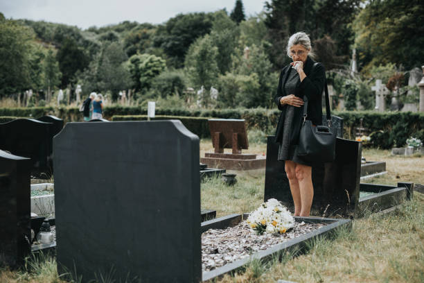 Widow woman visiting grave of lost relative, husband or child. in the rain under umbrella. Dark setting