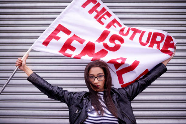 The present is female, the future is female Portrait of a woman holding a flag that reads "The future is female" protesting in the city womens rights stock pictures, royalty-free photos & images