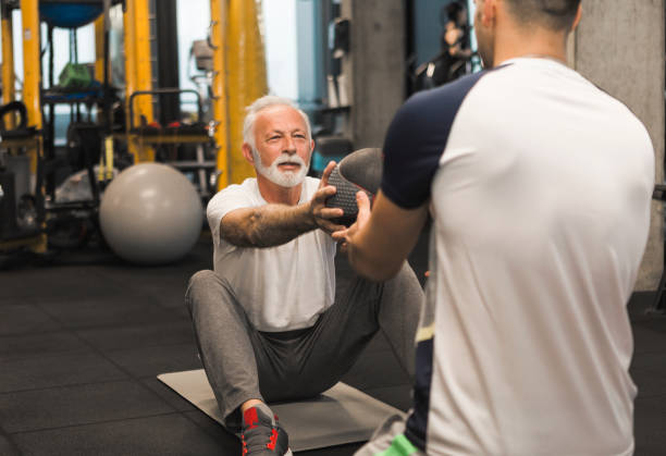 istock Senior man doing sit ups with trainer in gym 1074849076