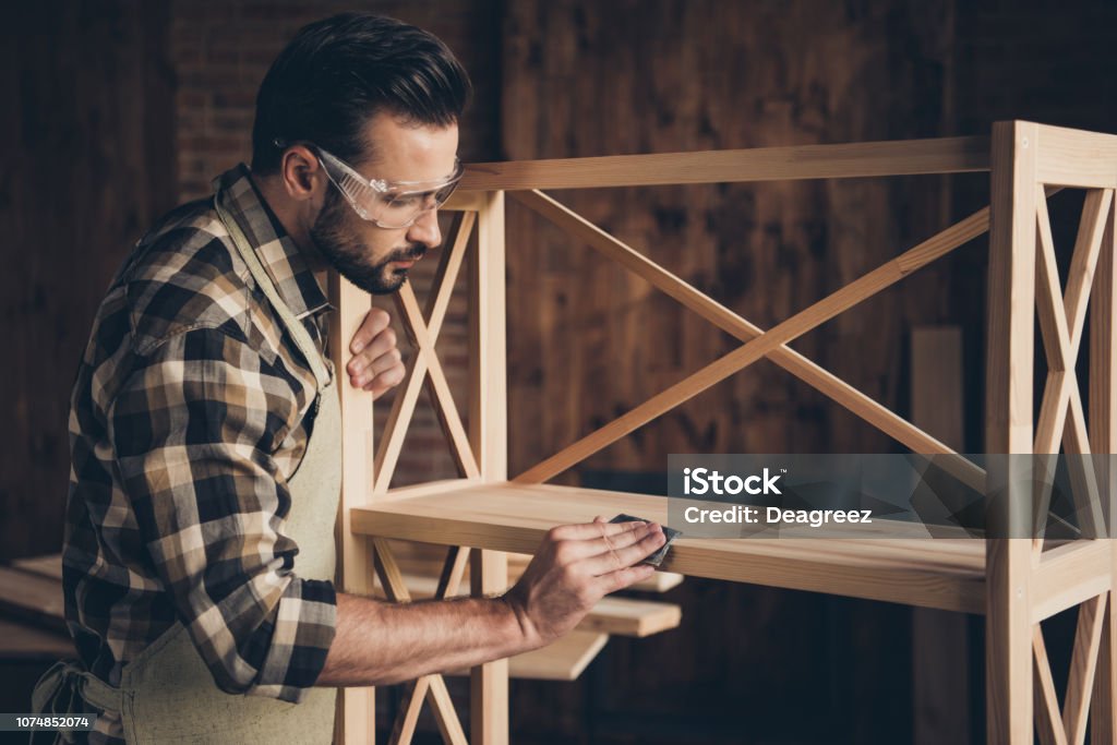 Plank panel wall unit wardrobe storage stand decorative creativi Plank panel wall unit wardrobe storage stand decorative creativity people person concept. Side profile closeup photo of serious stylish modern guy using abrasive paper for removing thorns splinters Carpenter Stock Photo