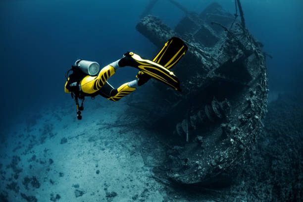 Yellow suited scuba diver exploring an overgrown shipwreck under the Red Sea Yellow suited scuba diver exploring a large overgrown shipwreck under the Red Sea. diving equipment stock pictures, royalty-free photos & images