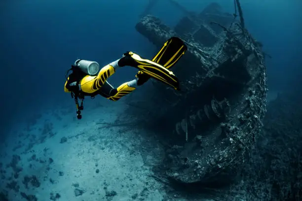 Yellow suited scuba diver exploring a large overgrown shipwreck under the Red Sea.