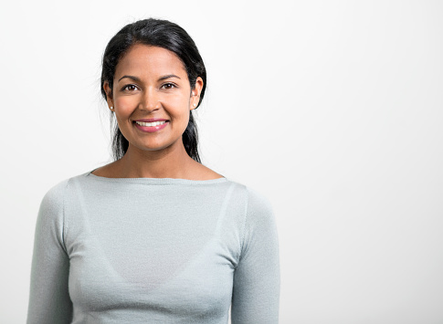 Portrait of Indian businesswoman smiling. Close-up of beautiful female professional is against white background. She is wearing smart casuals.