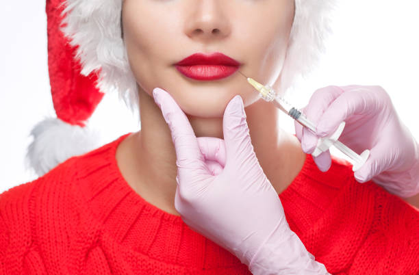 kosmetolog lekarz sprawia, że zastrzyk na ustach pięknej kobiety w kapeluszu świętego mikołaja. - christmas women human lips female zdjęcia i obrazy z banku zdjęć