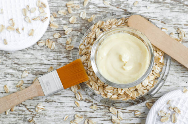 piccola ciotola di vetro con maschera facciale (idratante), burro per il corpo con estratto d'avena. ingredienti cosmetici naturali. sfondo in legno. vista dall'alto, copia spazio. - oat oatmeal rolled oats oat flake foto e immagini stock