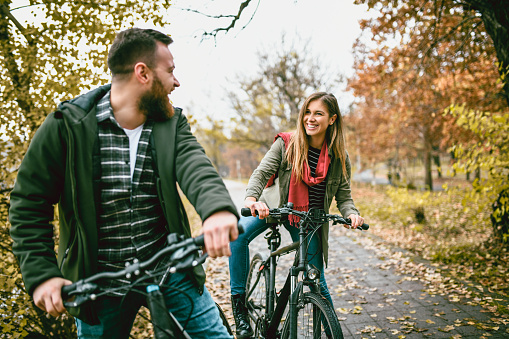 Young Cheerful Couple Taking a Bike Ride In Park In Autumn Ambient