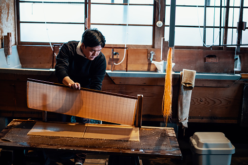 Mid adult man making paper using the traditional Japanese method of screening pulp and fiber.