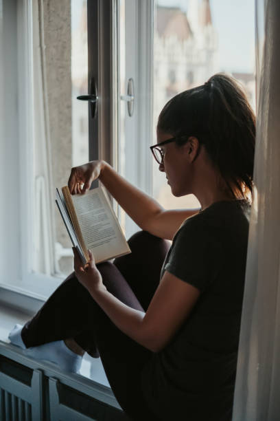 istock Brunette girl reading book on the window 1074897858
