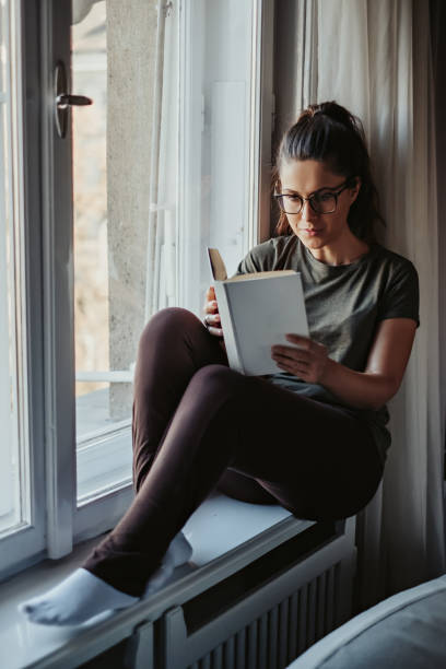 istock Serious girl reading book on the window 1074897860