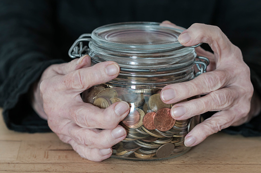 Hands of an old woman holding a mason jar with coins.