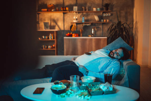 Overweight guy napping Overweight guy, lying on sofa and napping, with junk food in front of him. unhealthy living stock pictures, royalty-free photos & images