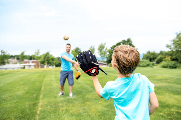 Handsome dad with his little cute sun are playing baseball on green grassy lawn A Handsome dad with his little cute sun are playing baseball on green grassy lawn baseball sport photos stock pictures, royalty-free photos & images