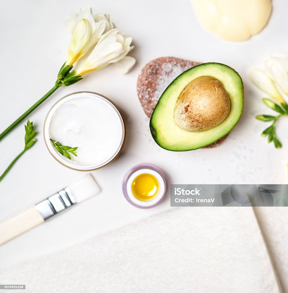 avocado and jar of cream oil lily flowers and sea salt soap white towel on a white background; Avocado skin care facial mask. Facial treatment concept. Flat lay, top view, copy space blogging Aging Process Stock Photo