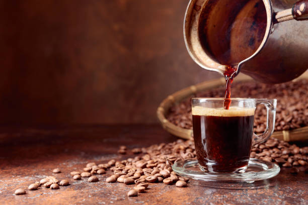 istock Black coffee is poured into a small glass cup from a old copper coffee maker. 1074924518