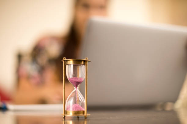 Hourglass on table with woman working on laptop in the background