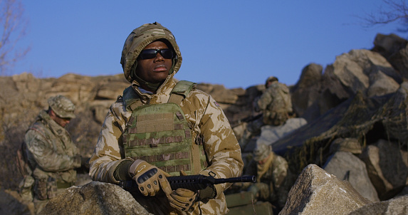 Medium shot of fully equipped and armed african american soldier wearing sunglasses during a mission