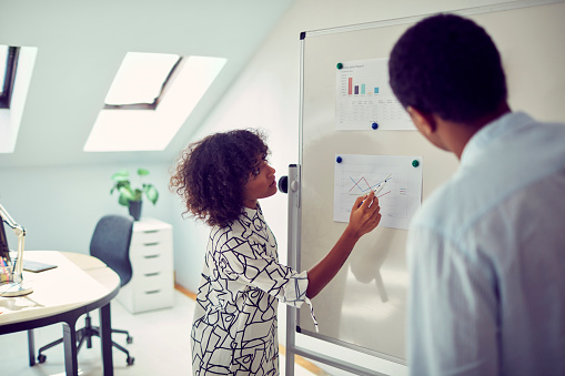 Business Meeting in the Office. African businesswoman and businessman standing and looking charts on whiteboard.