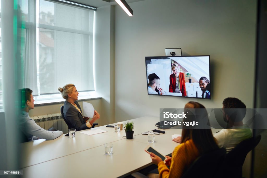 Business People Having a Video Call Business People Having a Video Call in Board Room. Sitting by the desk and talking with coworkers on lcd tv. Business Meeting Stock Photo