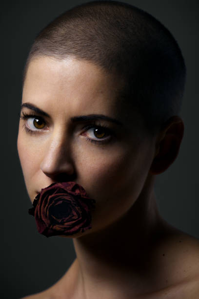 아름 다운 여성 암 환자 면도 머리와 그녀의 입에 장미. 암 금기, 평등 및 사회 개념에 의해 차별. - taboo 뉴스 사진 이미지