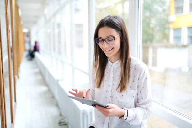 istock Close up of smiling Caucasian female student using tablet while standing next to noticeboard in college hall. 1074964186